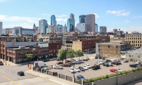 a parking lot with cars and The Paxon in the background